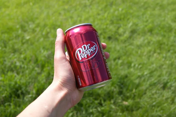 KHARKOV, UKRAINE - 12 Haziran 2020: El, yeşil çimenlerin arka planında Dr. Pepper 'ın metal kutusunu tutuyor.