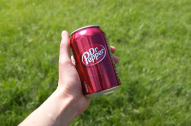 KHARKOV, UKRAINE - 12 Haziran 2020: El, yeşil çimenlerin arka planında Dr. Pepper 'ın metal kutusunu tutuyor.