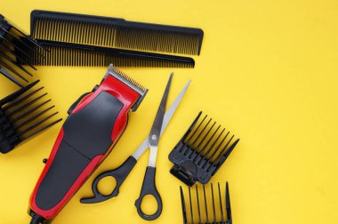 Hairdressers tool. Hair clipper close-up on a yellow background with nozzles of different sizes, scissors and combs. clipart