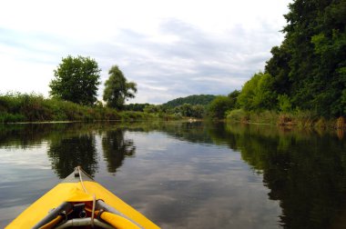 Resimli doğanın arka planında kano burnu. Yaz aylarında Seversky Donets nehrinin kıyısındaki ağaçlar boyunca sarı bir kanoda kürek çekiyorlar..
