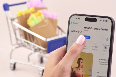 KHARKOV, UKRAINE - 18 Ağustos 2024: Akıllı telefonlu alışveriş arabası ekranda Mango uygulaması açık.