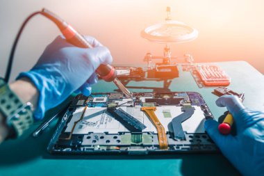 Asyalı teknisyenin labaratuvardaki demir lehimleyerek tableti tamir ettiği soyut görüntü. bilgisayar donanımı, cep telefonu, elektronik, onarım, güncelleme ve teknoloji kavramı.