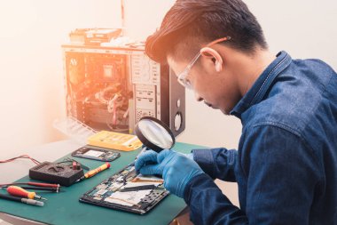 Asyalı teknisyenin laboratuvardaki büyüteçle tabletin içinde tamir ettiği soyut görüntü. bilgisayar donanımı, cep telefonu, elektronik, onarım, güncelleme ve teknoloji kavramı