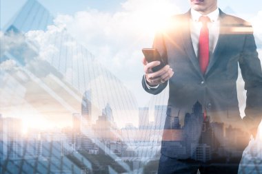 Gündoğumu sırasında akıllı telefon kullanan işadamının şehir görüntüsüyle çifte pozlama görüntüsü. Modern hayat, iş, şehir hayatı ve internet kavramı..