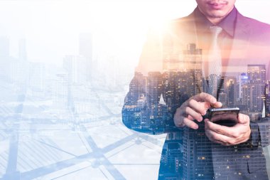 Gündoğumu sırasında akıllı telefon kullanan işadamının şehir görüntüsüyle çifte pozlama görüntüsü. Modern hayat, iş, şehir hayatı ve internet kavramı..