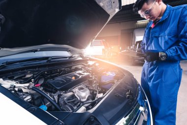 Asyalı teknisyen arabanın motorunu ve not listesini garajda analiz ediyor. otomotiv, onarım, mekanik, araç ve teknoloji kavramı.