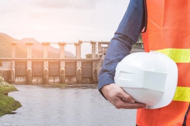 Miğfer tutan mühendisin ve hidroelektrik barajın soyut görüntüsü arka planda. temiz enerji, hidroelektrik, su yönetimi ve mühendislik kavramı