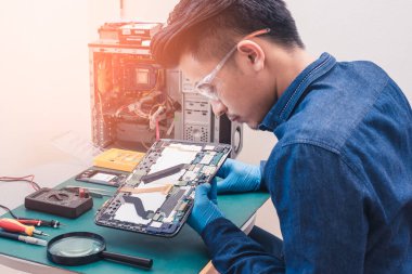 Asyalı teknisyenin laboratuvardaki büyüteçle tabletin içinde tamir ettiği soyut görüntü. bilgisayar donanımı, cep telefonu, elektronik, onarım, güncelleme ve teknoloji kavramı.