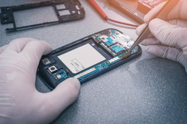 Laboratuvarda akıllı telefonun ve yeşil fotokopi alanının içinde tamirat yapan teknisyenin soyut görüntüsü arka plandır. akıllı telefon, elektronik, onarım ve teknoloji kavramı.