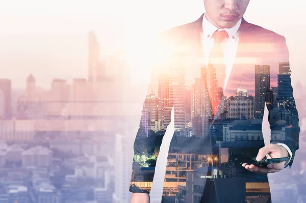 The double exposure image of the business man standing back during sunrise overlay with cityscape image. The concept of modern life, business, city life and internet of things.