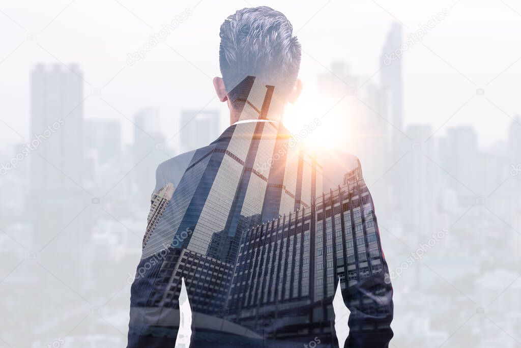 The double exposure image of the business man standing back during sunrise overlay with cityscape image. The concept of modern life, business, city life and internet of things.