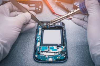Teknisyen, laboratuvarda lehimleyerek akıllı telefonun ana kartını onarıyor. bilgisayar donanımı, cep telefonu, elektronik, onarım, güncelleme ve teknoloji kavramı.
