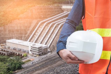 Miğfer tutan mühendisin ve hidroelektrik barajın soyut görüntüsü arka planda. temiz enerji, hidroelektrik, su yönetimi ve mühendislik kavramı