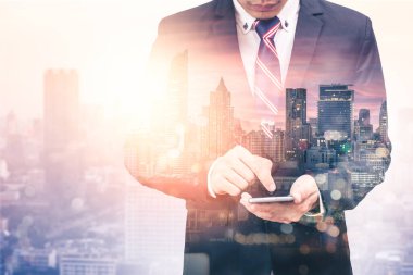 Gündoğumu sırasında akıllı telefon kullanan bir iş adamının şehir görüntüsüyle çifte pozlama görüntüsü. Modern hayat, iş, şehir hayatı ve internet kavramı..