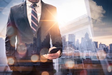 Gündoğumu sırasında akıllı telefon kullanan bir iş adamının şehir görüntüsüyle çifte pozlama görüntüsü. Modern hayat, iş, şehir hayatı ve internet kavramı..