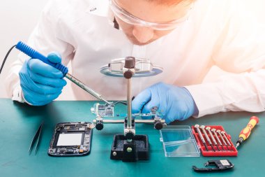 Asyalı teknisyen laboratuvarda lehim ve büyüteç kullanarak akıllı telefonun ana kartını tamir ediyor. bilgisayar donanımı, cep telefonu, elektronik, onarım, güncelleme ve teknoloji kavramı.
