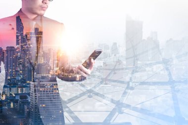 Gündoğumu sırasında akıllı telefon kullanan işadamının şehir görüntüsüyle çifte pozlama görüntüsü. Modern hayat, iş, şehir hayatı ve internet kavramı..