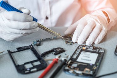 Asyalı teknisyen laboratuvarda lehim ve büyüteç kullanarak akıllı telefonun ana kartını tamir ediyor. bilgisayar donanımı, cep telefonu, elektronik, onarım, güncelleme ve teknoloji kavramı.