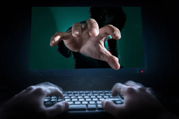 The abstract image of the hacker stretch out one\'s hand out of the monitor and someone typing on the front. The concept of hacker, cyber security, data theft and data protections.