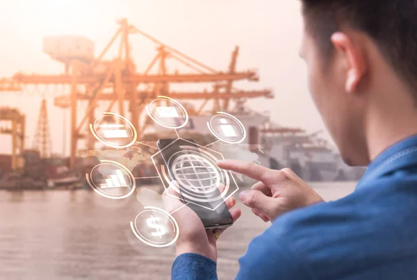 İş adamının soyut görüntüsü akıllı telefonundaki hologramı ve bulanık limanı gösteriyor. Nesnelerin ve lojistik şeylerin iletişim ağı konsepti