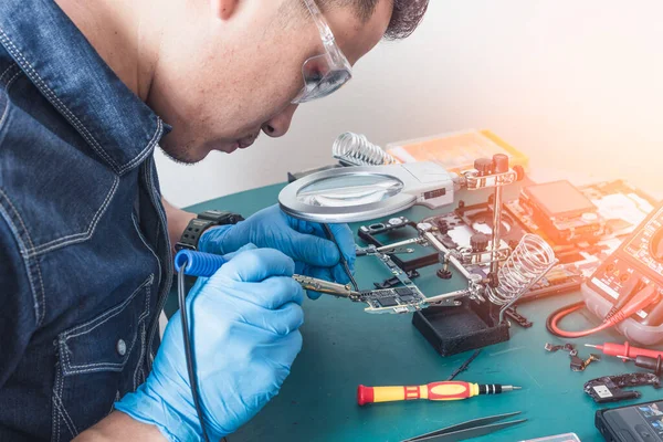 The asian technician repairing the smartphone\'s motherboard by soldering in the lab. the concept of computer hardware, mobile phone, electronic, repairing, upgrade and technology.