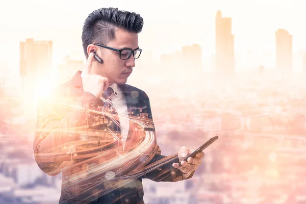 The double exposure image of the business man using a smartphone during sunrise overlay with cityscape image. The concept of modern life, business, city life and internet of things.