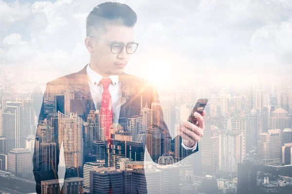 The double exposure image of the businessman using a smartphone during sunrise overlay with cityscape image. The concept of modern life, business, city life and internet of things.