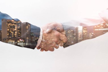İş adamının gün doğumunda bir diğeriyle tokalaşırken çekilmiş çifte pozlama görüntüsü şehir görüntüsüyle örtüşüyor. Modern hayat, iş, şehir hayatı ve takım çalışması kavramı.