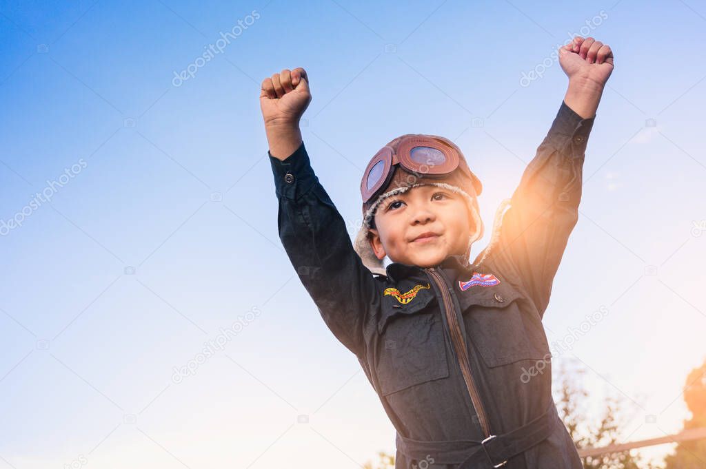 the boy in the pilot suit raises his hand up during sunrise and copy space.