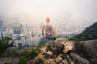 Kameralı bir erkek uçurumun kenarında durup şehri gözetliyor.