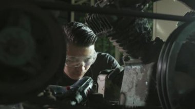 Atölyedeki tamirci paslı eski hava kompresörünü tamir ediyor.