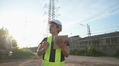 Mühendisin 4K görüntüsü inşaat alanındaki yüksek voltaj kulesini inceliyor. mühendislik, elektrik, inşaat ve teknoloji kavramı. 