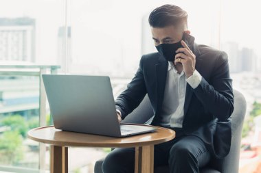 İş adamı koruyucu yüz maskesi takıyor ve koronavirüs salgını sırasında çalışıyor. Koronavirüs, salgın, girişimci ve iş dünyası kavramı.