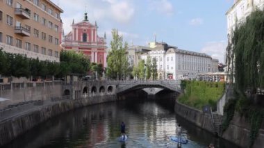 Ljubljana, Slovenya - 10 Ağustos 2020: Slovenya 'nın başkenti Ljubljana' nın merkezindeki Tromostovje 'ye doğru Ljubljanica nehrinde kürek çeken bir grup genç