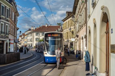 Cenevre, İsviçre - 9 Eylül 2025: Tarihi binalarla çevrili Carouge kasabasındaki modern bir tramvay, yakınlarda yayalar ve açık mavi bir gökyüzü