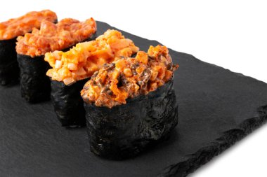 Siyah seramik masa tabağında dört Gunkan suşi rulosu. Baharatlı soslu somon, ton balığı, yılan balığı ve tobiko ile lezzetli Japon mutfağı. Beyaz arka planda izole yiyecekler.