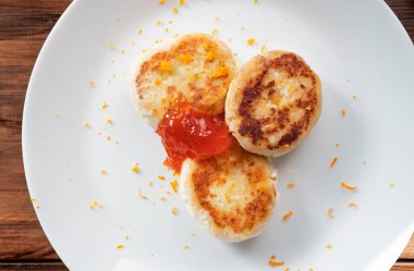 Portakal aromalı süzme peynir krepleri ve beyaz tabakta kayısı reçeli. Ahşap kırsal masa arka planında servis edilmiş. Diyet konseptinde lezzetli yüksek proteinli kahvaltı..