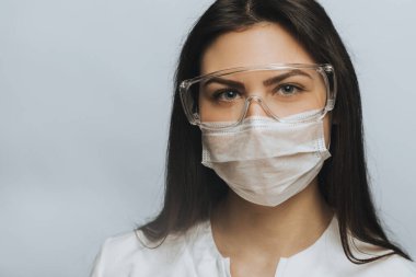 COVID-19 Coronavirus salgını. Ciddi bir doktor. Hastanede cerrahi maske ve koruyucu gözlük takarak portre yakın plan. İlham verici güven ve profesyonellik.