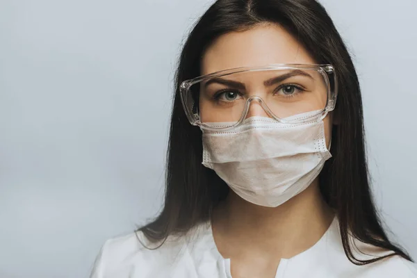 COVID-19 Coronavirus salgını. Ciddi bir doktor. Hastanede cerrahi maske ve koruyucu gözlük takarak portre yakın plan. İlham verici güven ve profesyonellik.
