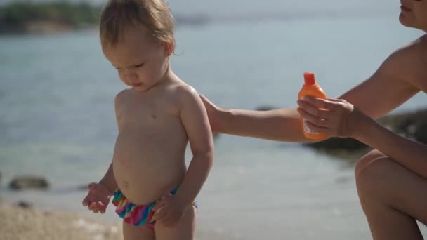 Мама смазывает свою двухлетнюю дочь солнцезащитным кремом — стоковое видео