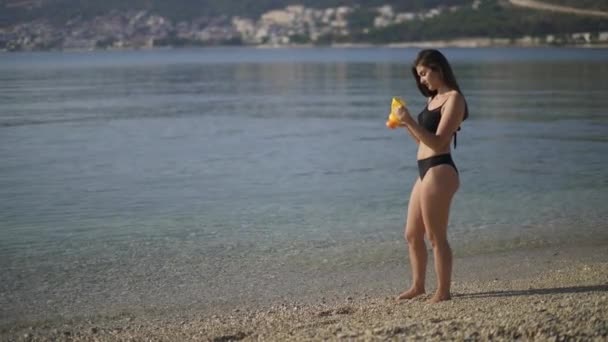 Mooi meisje smeert zichzelf in met zonnebrandcrème op het strand. Ochtend op een verlaten strand. — Stockvideo