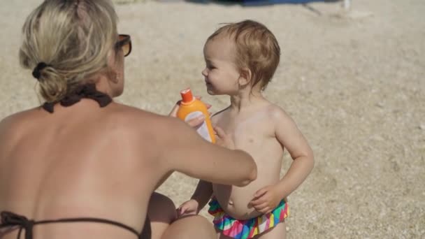 Мама смазывает свою двухлетнюю дочь солнцезащитным кремом — стоковое видео