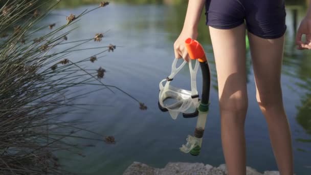 Nastolatek trzyma maskę z rurką do pływania. Facet stoi na tle jeziora, morza.. — Wideo stockowe