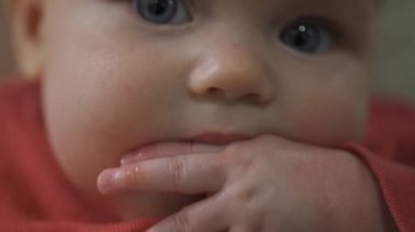 Bir yaşındaki küçük bir kız parmaklarını emiyor. Dişleri delinmiş. Çocuk kameraya bakıyor..
