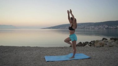 Güzel kız ısınıyor ve deniz kenarında yoga yapıyor. Spor, yoga, plaj..
