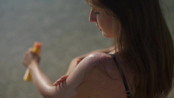 아름다운 소녀는 해변에 서 있는 선크림으로 자기 자신을 찌르고 있다. 어깨를 가까이 하라. — 비디오