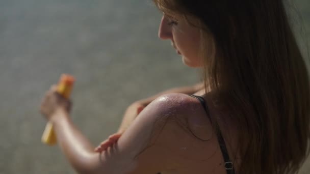 Hermosa chica se unta con protector solar de pie en la playa. Hombro de cerca . — Vídeo de stock