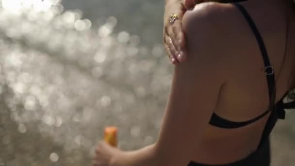Vacker flicka smetar sig med solkräm stående på stranden. Axeltätning. — Stockvideo
