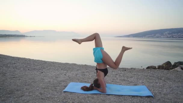 Schöne Mädchen wärmt sich auf und praktiziert Yoga am Meer. Sport, Yoga, Strand. — Stockvideo