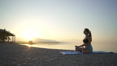 Güzel kız ısınıyor ve deniz kenarında yoga yapıyor. Spor, yoga, plaj..